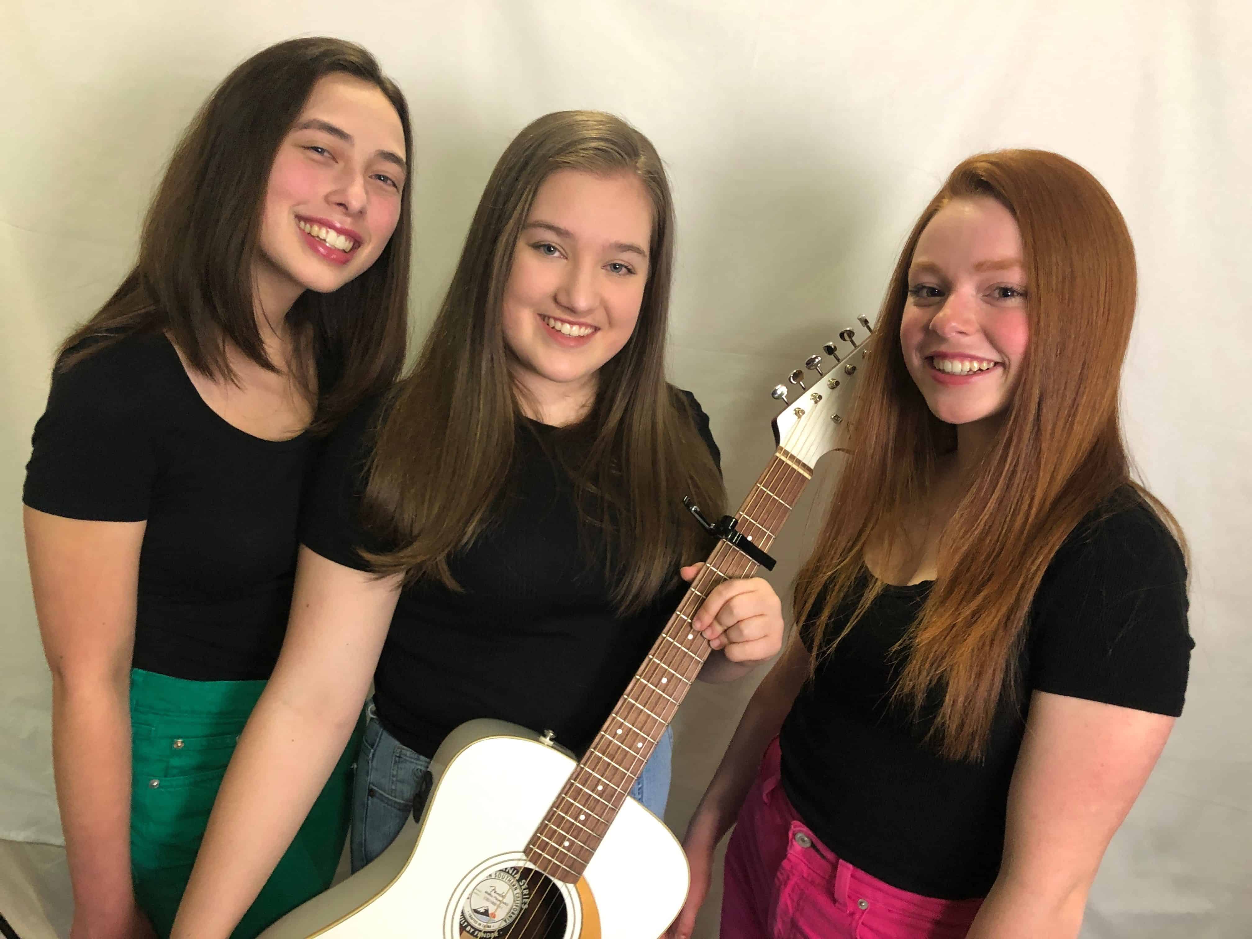 photo of three smiling women musicians and guitar